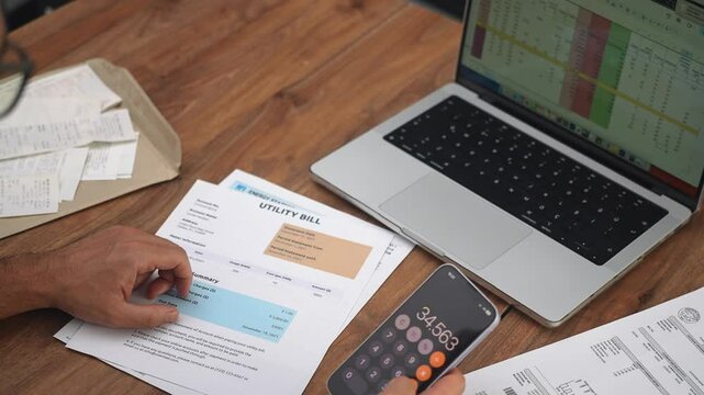 Male office worker inspects utility bills calculating combined expenses, accountant compiles report about household expenditure using phone calculator slow motion