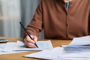 Closeup of unrecognizable woman sitting at desk at home, studying draft of agreement on paper copy...