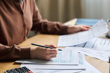 Closeup of unrecognizable young woman sitting at desk in office, studying draft of agreement on...