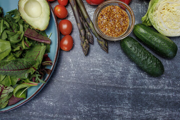 Fresh vegetables and herbs in a plate on a dark surface top view. avocado, cherry tomatoes, bell peppers, asparagus, parsley and grain mustard, kale. healthy eating concern