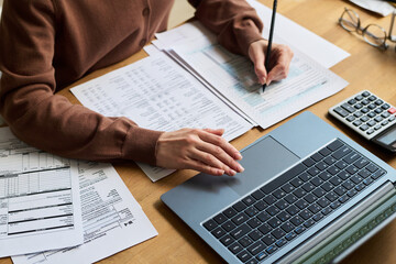 High angle closeup of hands of young woman calculating domestic expenses and utility invoices using...