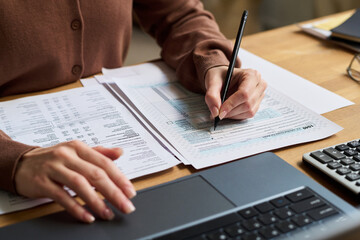 Hands of young woman calculating expenses using laptop, while sitting at desk and managing budget