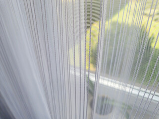 Soft sheer curtains filter natural light, creating a warm atmosphere inside a modern home. The scene captures a glimpse of greenery outside, enhancing relaxation.