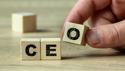A hand rearranging wooden blocks displaying the letters 'C', 'E', and 'O' on a wooden surface, symbolizing leadership and corporate management in a business context.