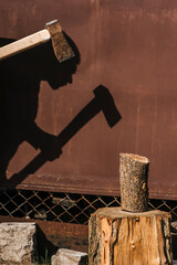 Photo of silhouette, shadow on wall of adult male strong lumberjack chopping log on stump with axe...