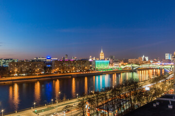 Obraz premium The skyline of Moscow glows at night with colorful lights reflecting in the river. Busy streets and bridges show the city's vibrant nightlife and urban energy.