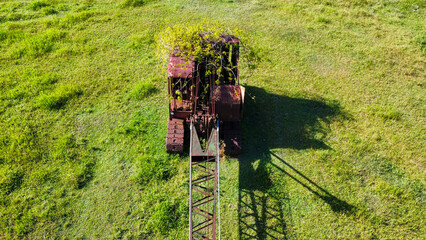 Abandoned crane on a meadow while nature is taking it back, seen from above