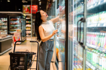 Elegant woman choosing groceries from refrigerated section in supermarket
