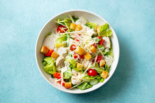 Caesar salad with chicken in a white bowl. Blue background. Close up. Top view.