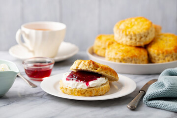 Scones with jam, clotted cream and cup of tea on marble table. Grey background. Close up.