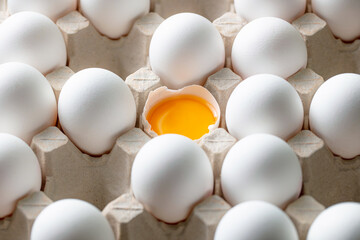 Eggs arranged in a cardboard carton with one egg cracked open, revealing vibrant yellow yolks. The...