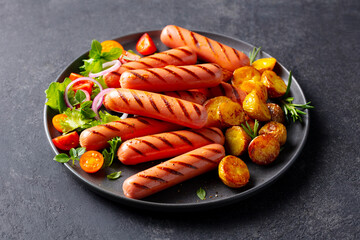 Grilled Sausages and Potatoes on Plate with Vegetables. Grey background. Close up.