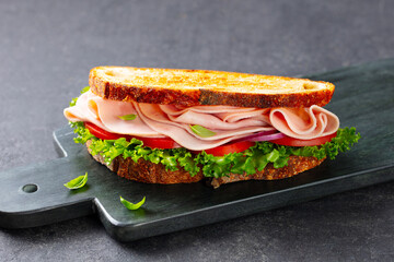 Ham sandwich, toast with green salad, fresh salad and tomatoes on a black marble board. Grey background. Close up.