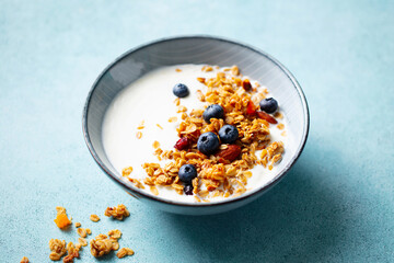 Healthy breakfast. Oat granola with fresh blueberries and milk in a bowl. Blue background. Close up.