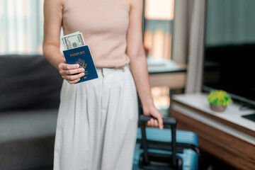Tourist woman is holding United States passport and dollars with suitcase in hotel room, ready for vacation