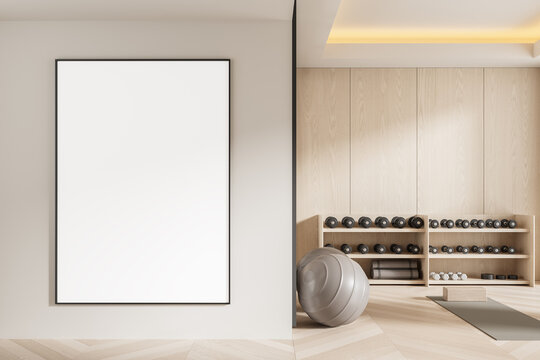 Blank poster mockup on white wall in modern minimalist home gym interior with wooden accents, yoga mat, fitness ball, and dumbbells. 3D Rendering. 3D Rendering