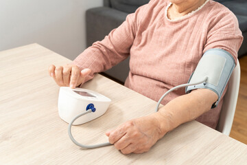 Elderly woman using a digital tensiometer, monitoring her blood pressure at home
