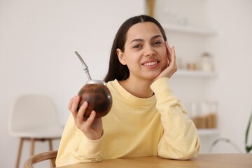 Woman drinking traditional yerba mate tea at table indoors