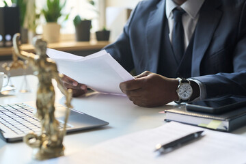 Unrecognizable Black male legal attorney working in office, looking through copy of contract