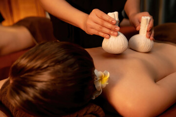 Hot herbal ball spa massage body treatment, masseur gently compresses herb bag on couple customer...