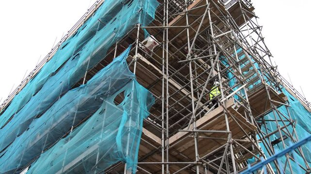 Workers walking up the scaffolding covering a large building