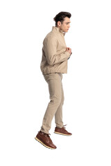 Naklejka premium side view of casual young man in beige jacket jumping up in the air
