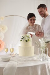 Married couple cutting delicious wedding cake with knife at table indoors