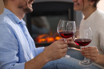 Couple clinking glasses of wine near fireplace at home, closeup