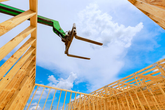 Workers are assembling structure with telehandler crane lifting wooden beams under bright sky with clouds