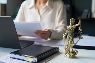 Bronze Lady Justice statuette on desk of attorney in law firm, holding scales and sword, and female...