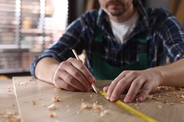 Man measuring plank with tape and pencil at wooden table indoors, closeup