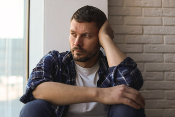 Depressed man sitting near window at home