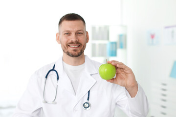 Nutritionist with green apple and stethoscope in clinic, selective focus