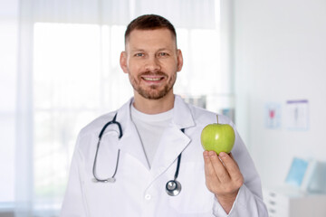 Nutritionist with green apple and stethoscope in clinic, selective focus