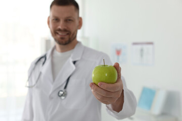 Nutritionist with green apple and stethoscope in clinic, selective focus