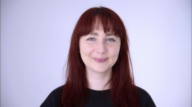 Portrait of a young woman with blue eyes, red hair in a black baize smiling and laughing on a light background.