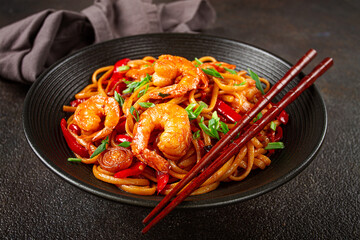 udon stir-fry shrimp noodles with red bell pepper and green onion, served in a black bowl, with...
