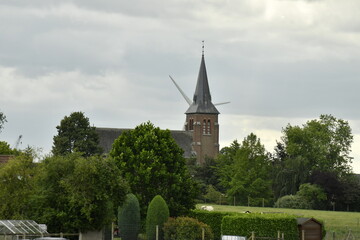 L'Église Saint-Jean l'Évangéliste derrière un bosquet et les pales d'une éolienne plus loin 