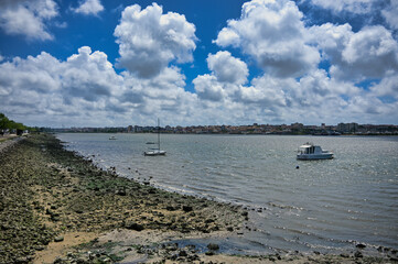 Scenic riverbank and moored boats in Seixal, Portugal, with clouds, calm waters and a view of the opposite shore on a bright day.