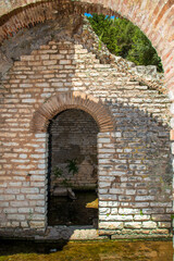Fototapeta premium Sunlit ancient limestone archway at the edge of a reflective water channel within the archaeological ruins of Butrint in southern Albania