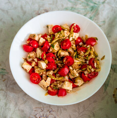 Crisp chopped Greek salad of cherry tomatoes, feta cheese cubes, cucumber ribbons and red onion in oregano-infused olive oil