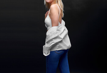 Portrait of sexy young woman in white busglatter with white shirt posing on dark background. Advertising trend.