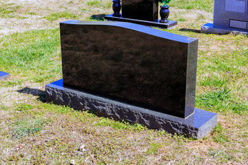 Polished black gravestone is positioned on green grass in peaceful cemetery under bright sunlight.