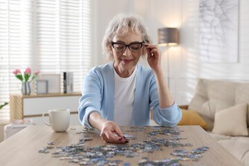 Woman solving jigsaw puzzle at wooden table indoors