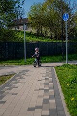 Small girl child learning to drive a balance bike with pink helmet on safe bicycle path in sunny summer day