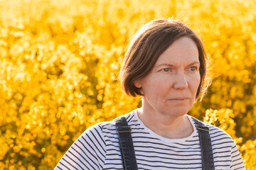 Portrait of beautiful adult female farmer standing in blooming canola plantation field on sunny...