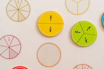 Educational math tools displayed on a white surface showcasing various fractions and pie chart...