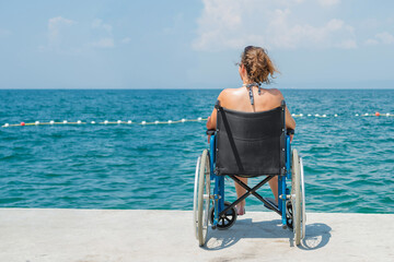 Smiling woman in a bikini, sitting relaxed in her blue wheelchair by the seaside, enjoying the sun...
