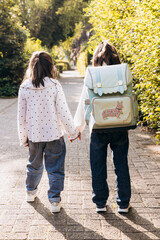 Two children walking hand in hand along a sunlit pathway surrounded by lush greenery, enjoying a...