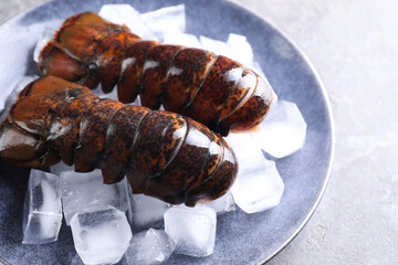Raw lobster tails with ice on grey table, closeup